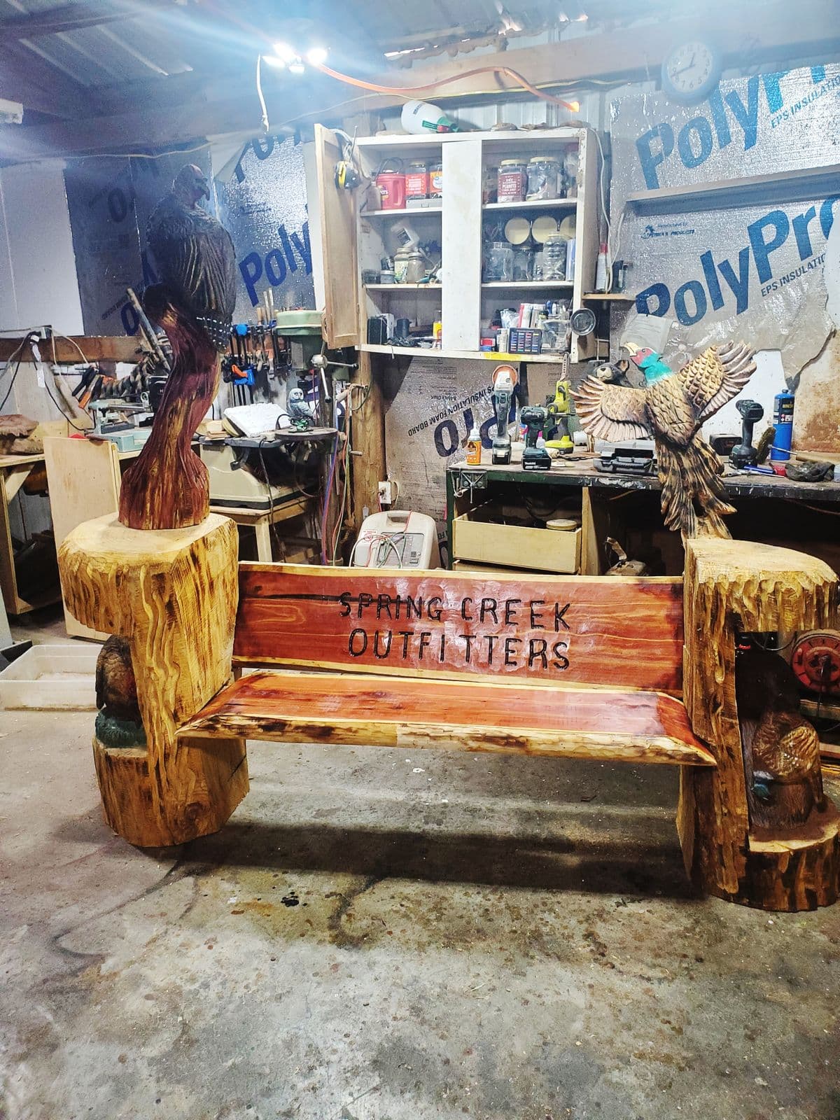Cedar bench lettered Spring Creek Outfitters with a hawk and a flying turkey carved on the posts