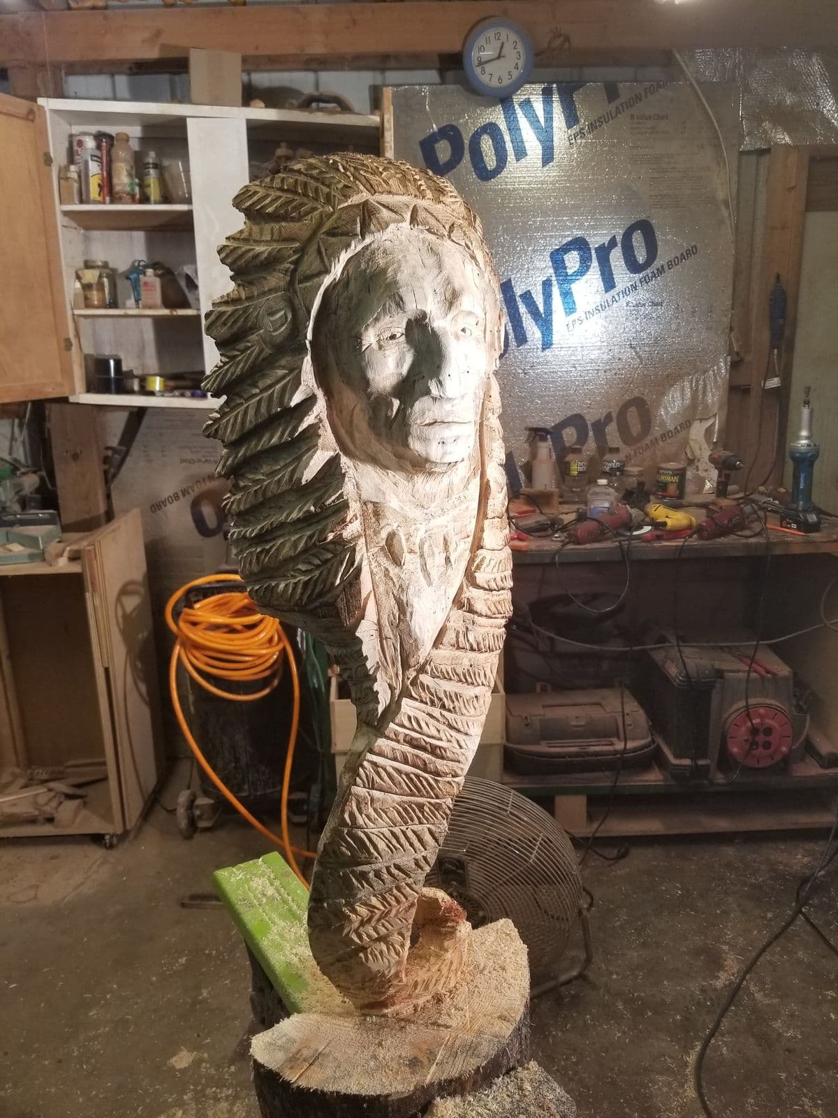 A tall carving of a face in a feathered headdress, unpainted and in progress in the workshop