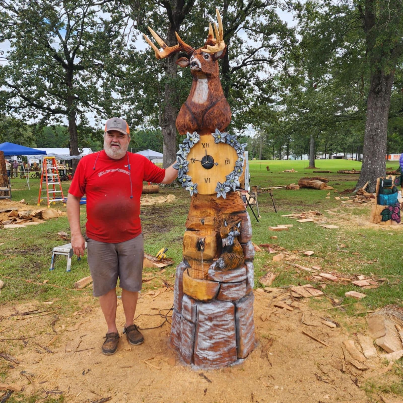 Tall carving of a whitetail buck above a working clock, shown at an outdoor carving event