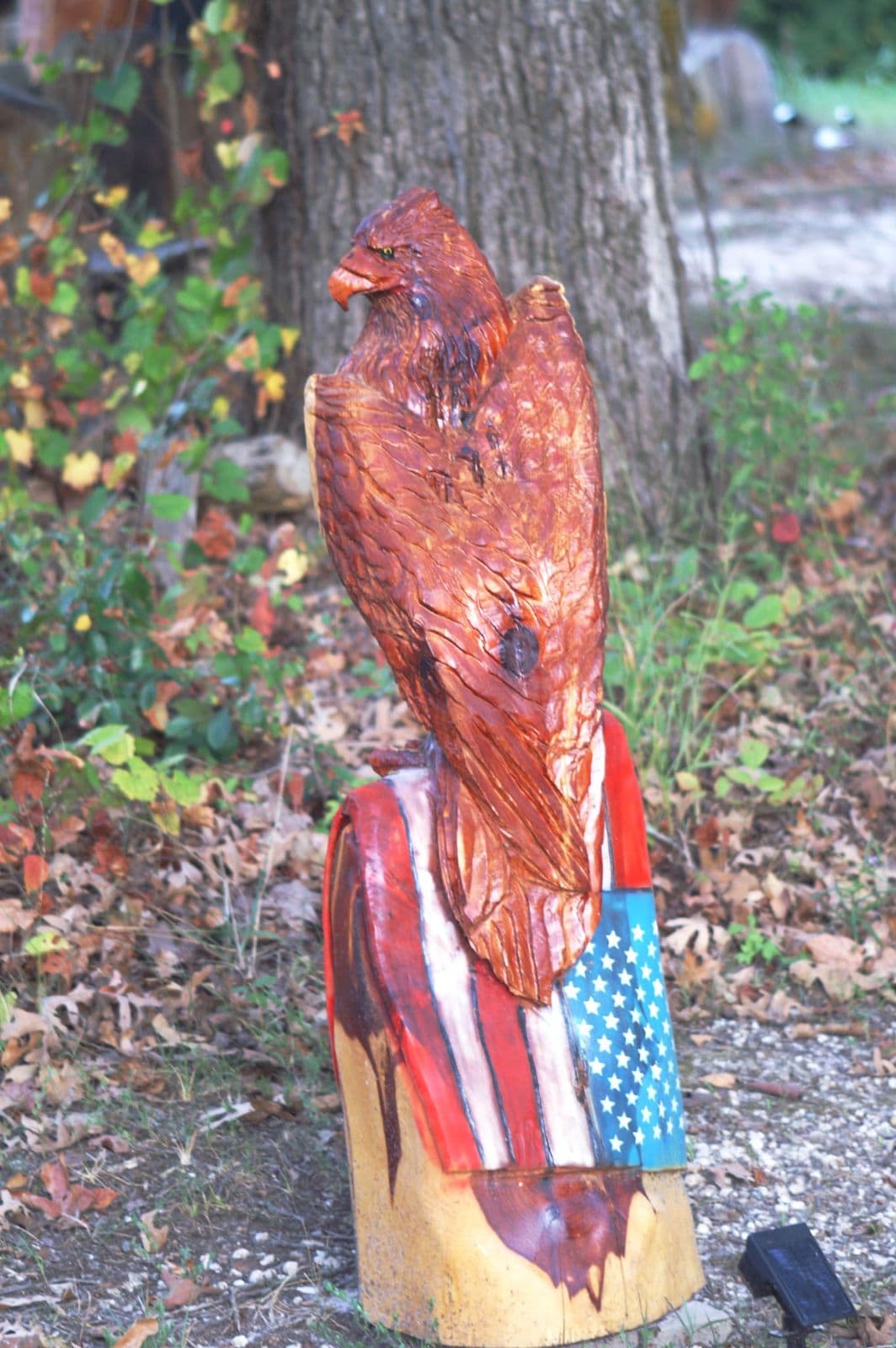 Cedar eagle perched on a stump draped with a painted American flag