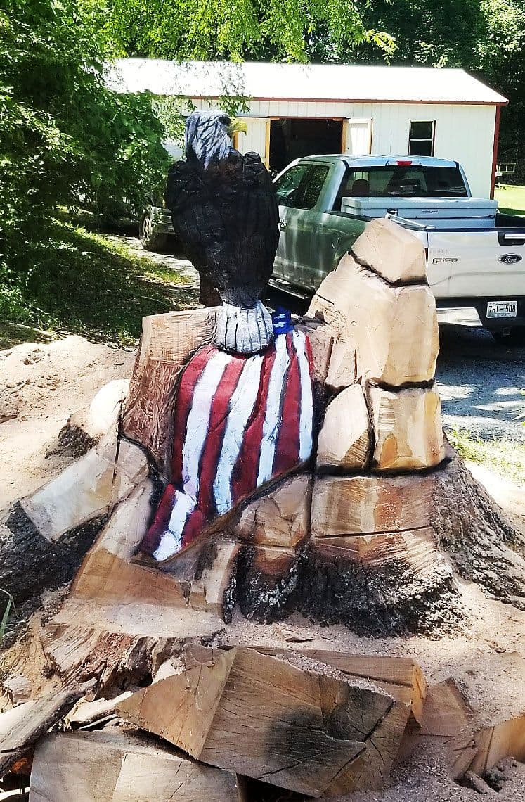 Wide stump mid-carve showing a bald eagle and a painted American flag