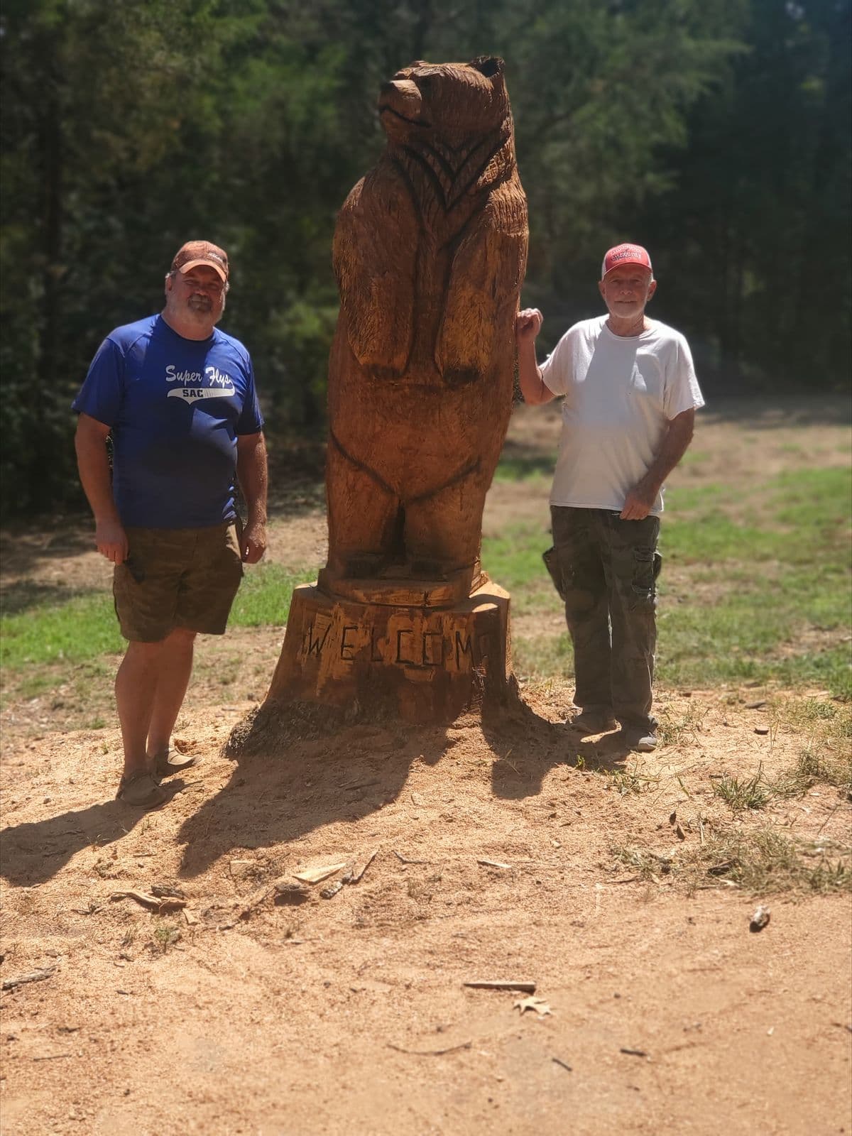 Large standing bear carved from a rooted stump, with two men beside it for scale